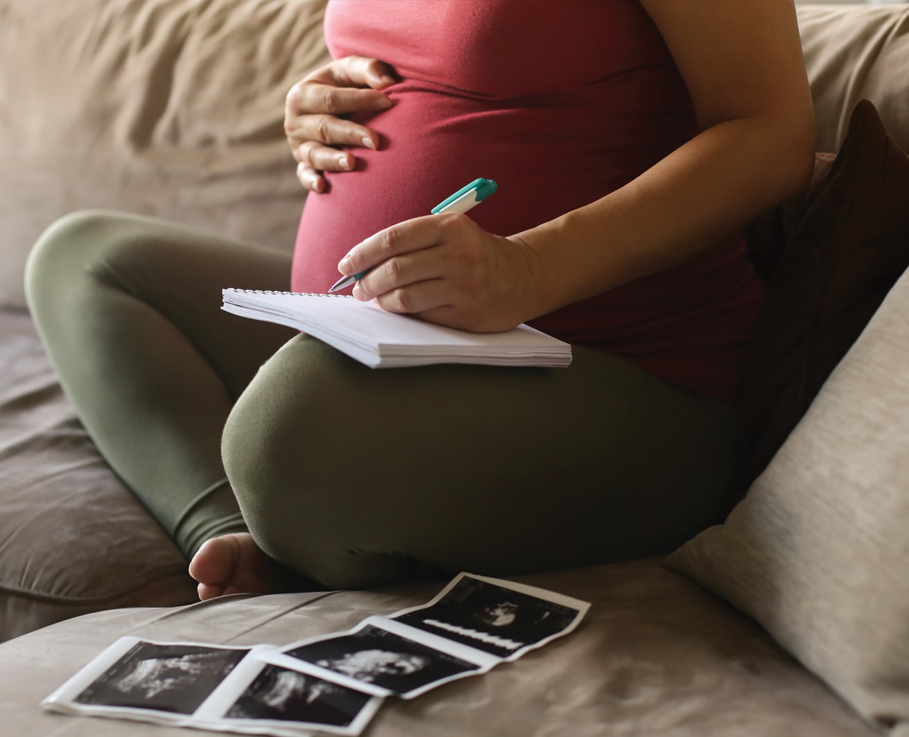 Pregnant woman sitting on a couch, writing in a notebook, with pictures of a sonogram